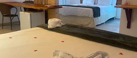 A hotel room with a bed, a wooden desk, a chair, a small refrigerator, and a mirror.