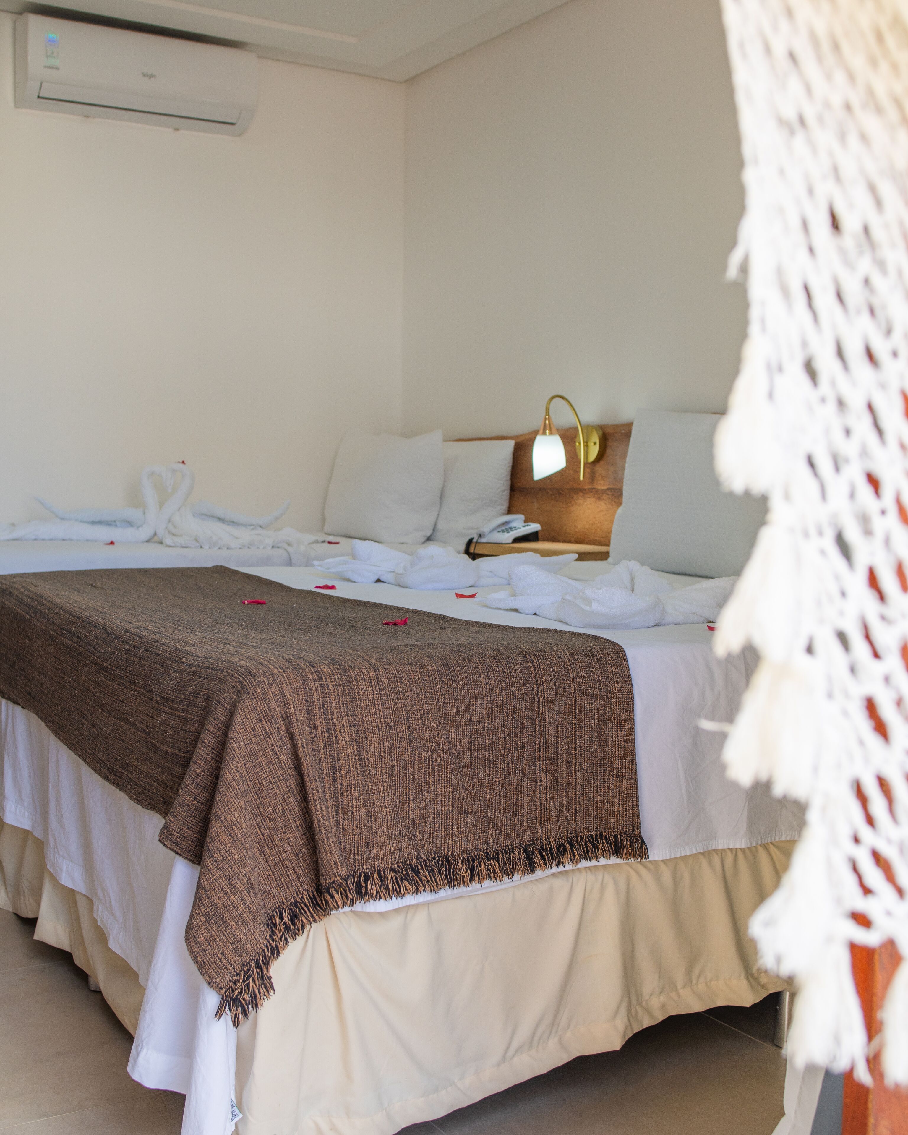 A hotel room with a bed, a bedside lamp, a phone, and a wall-mounted air conditioner.