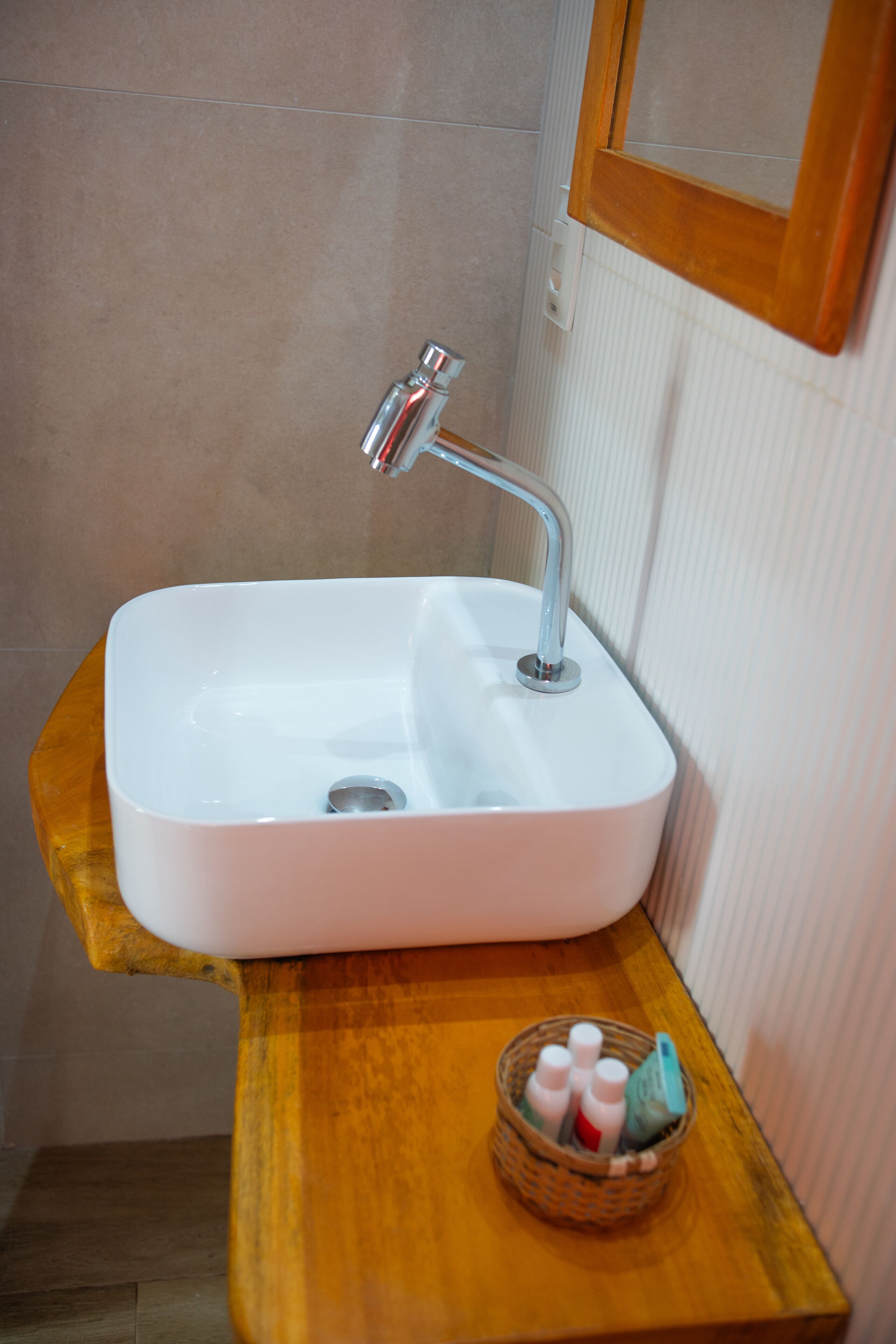 A bathroom with a white sink, wooden countertop, and a small basket with toiletries.