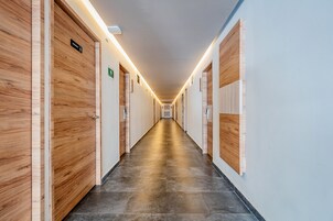 Un largo pasillo bien iluminado con puertas de madera a ambos lados, que conduce a habitaciones.