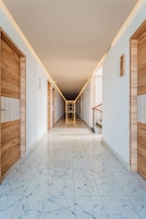 Un largo pasillo estrecho con puertas de madera a ambos lados, suelo de baldosas y una escalera al final.