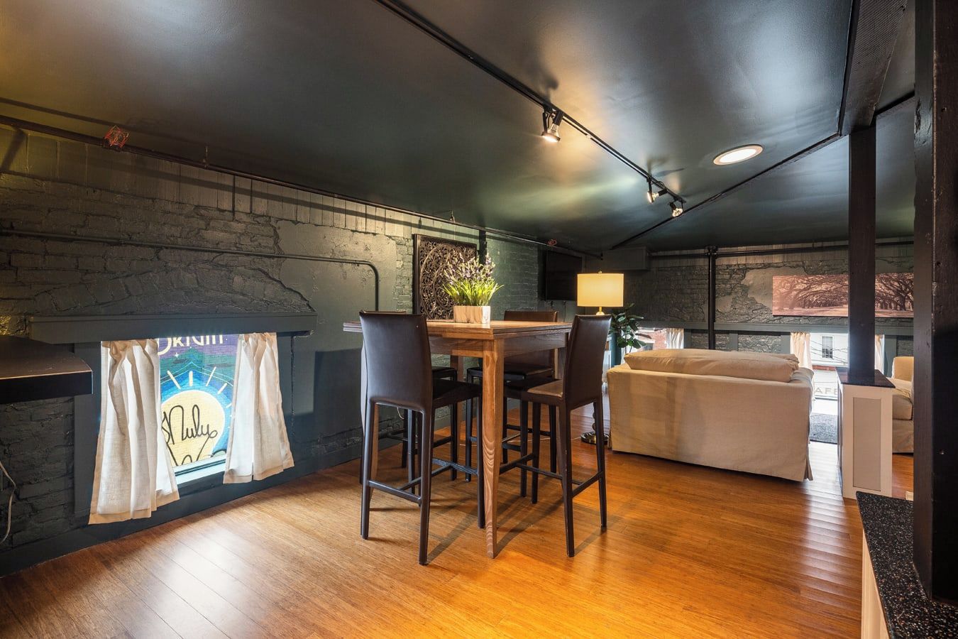 Una habitación acogedora con suelo de madera, una mesa de comedor con sillas, un sofá y una chimenea con un cartel decorativo.