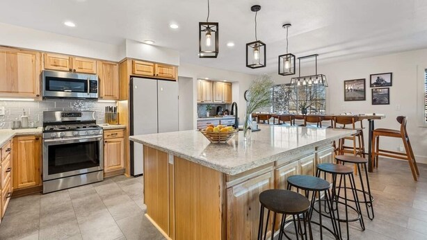 Cocina moderna con armarios de madera, electrodomésticos de acero inoxidable y una isla central con taburetes de bar.