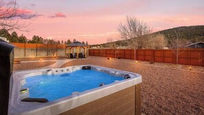 Un patio trasero con un jacuzzi, un pabellón de madera y una cerca de madera.