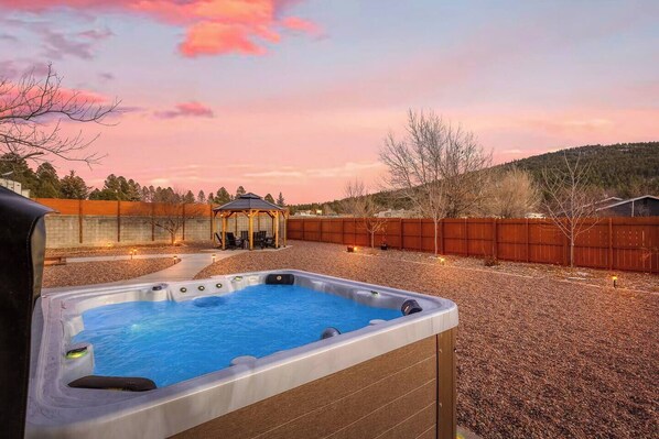 Un patio trasero con un jacuzzi, un pabellón de madera y una cerca de madera.