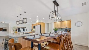 Una cocina moderna con una isla central, taburetes de madera, iluminación colgante y armarios de madera.