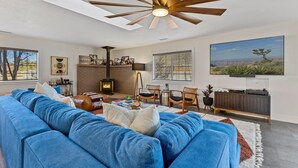 Una sala de estar con un sofá azul, una chimenea, un ventilador de techo y un ventanal grande.