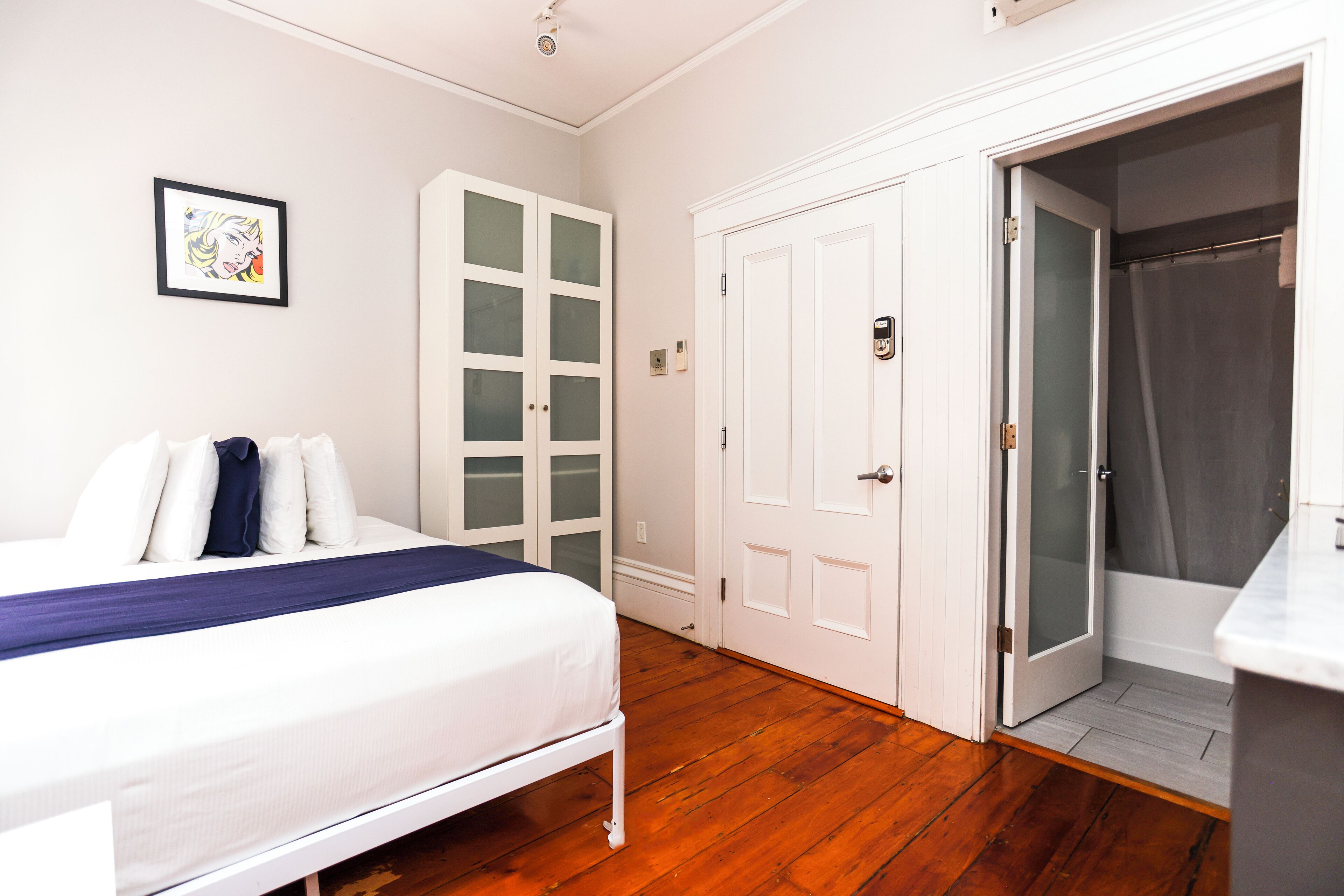 A bedroom with a bed, a wardrobe, and a shower area.