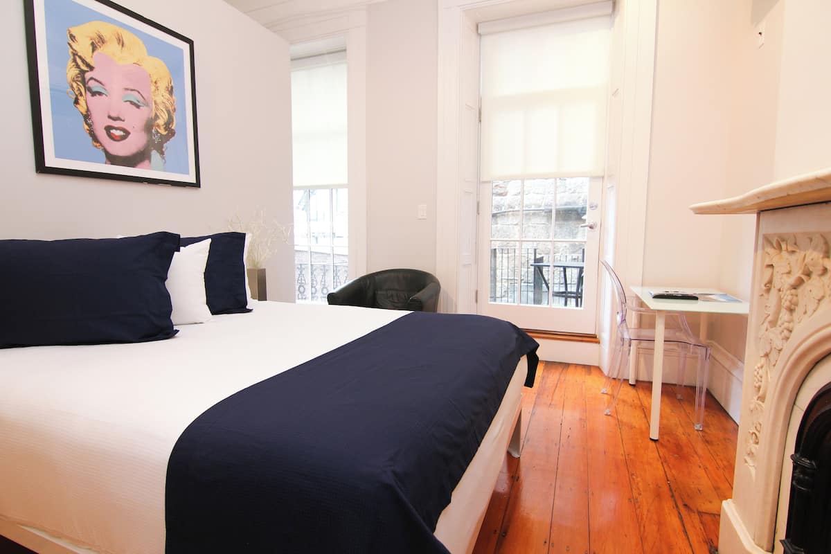A bedroom with a bed, a chair, a small table, and a fireplace.