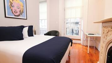 A bedroom with a bed, a chair, a small table, and a fireplace.