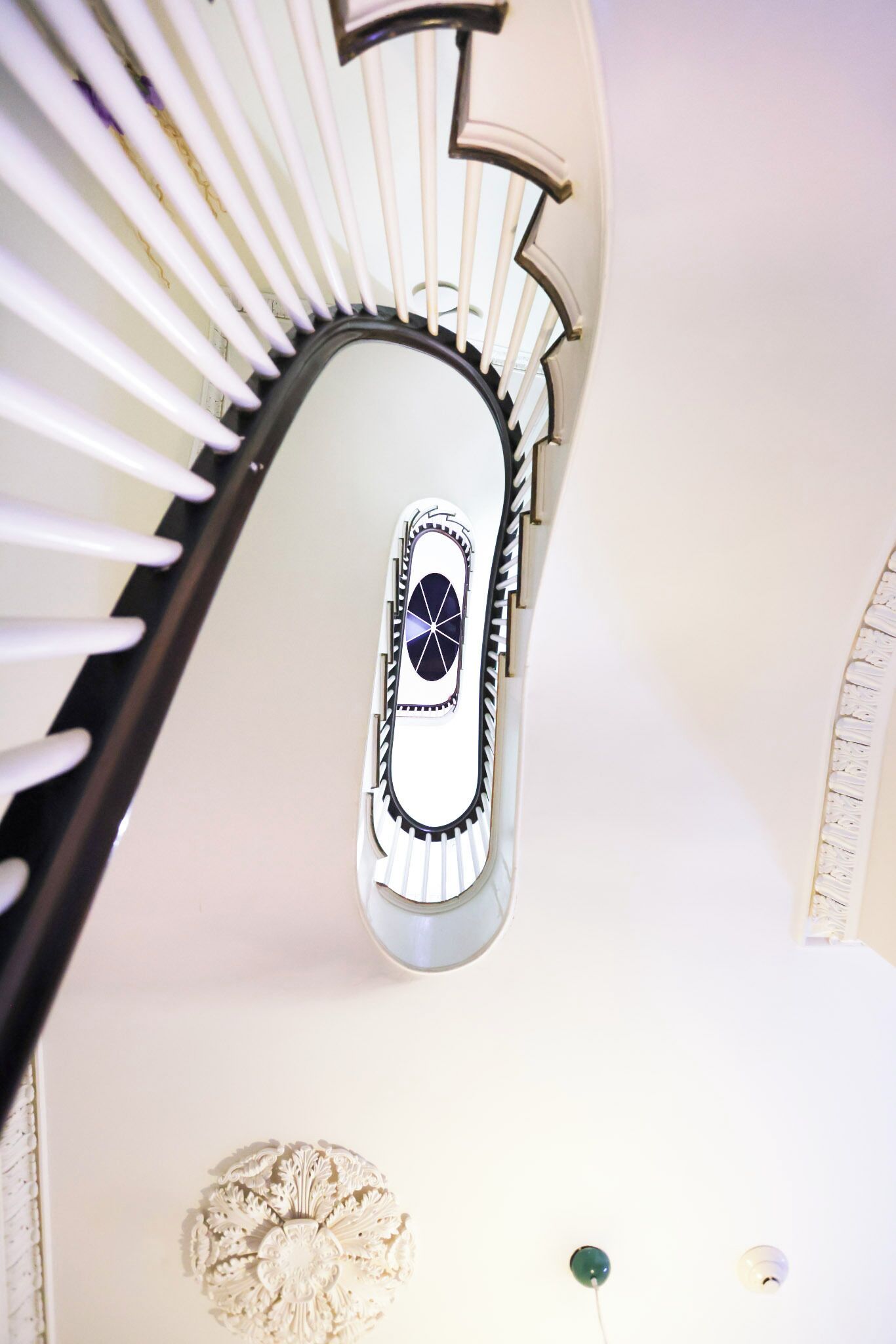 A spiral staircase with a white railing and a decorative wall panel at the bottom.