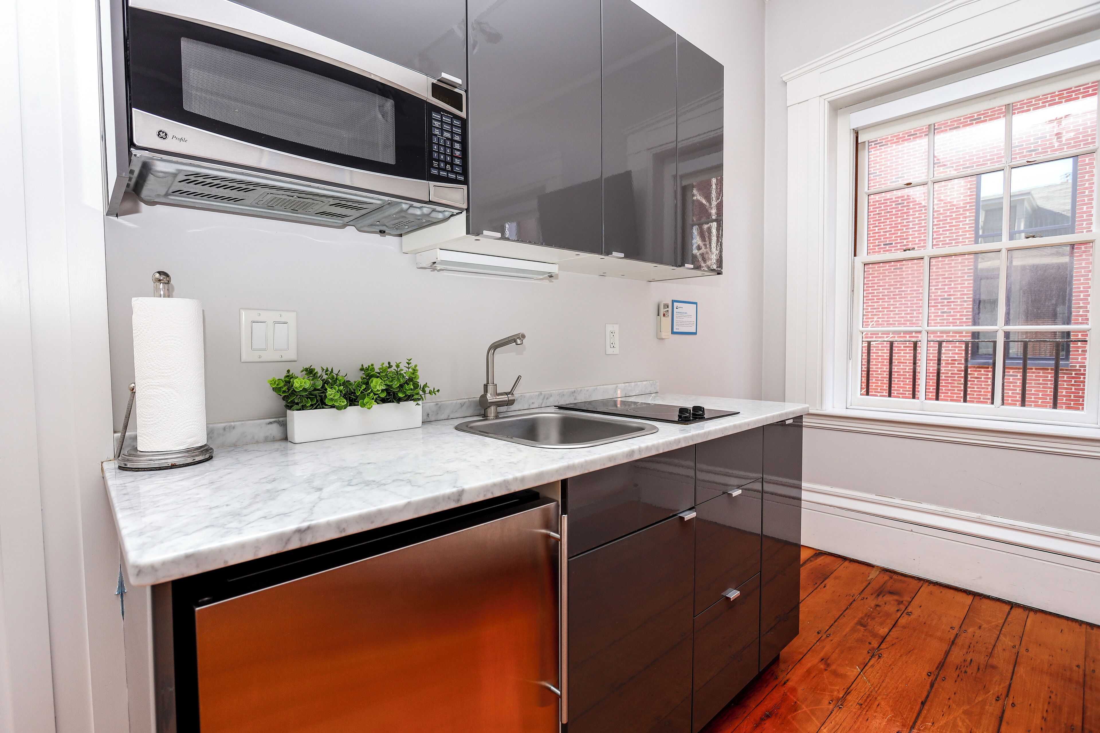 A kitchen with a stainless steel sink, a microwave, and a window with a view of a brick building.