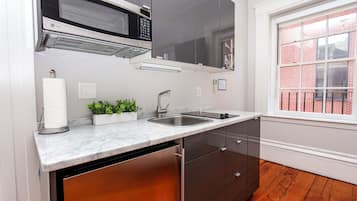 A kitchen with a stainless steel sink, a microwave, and a window with a view of a brick building.
