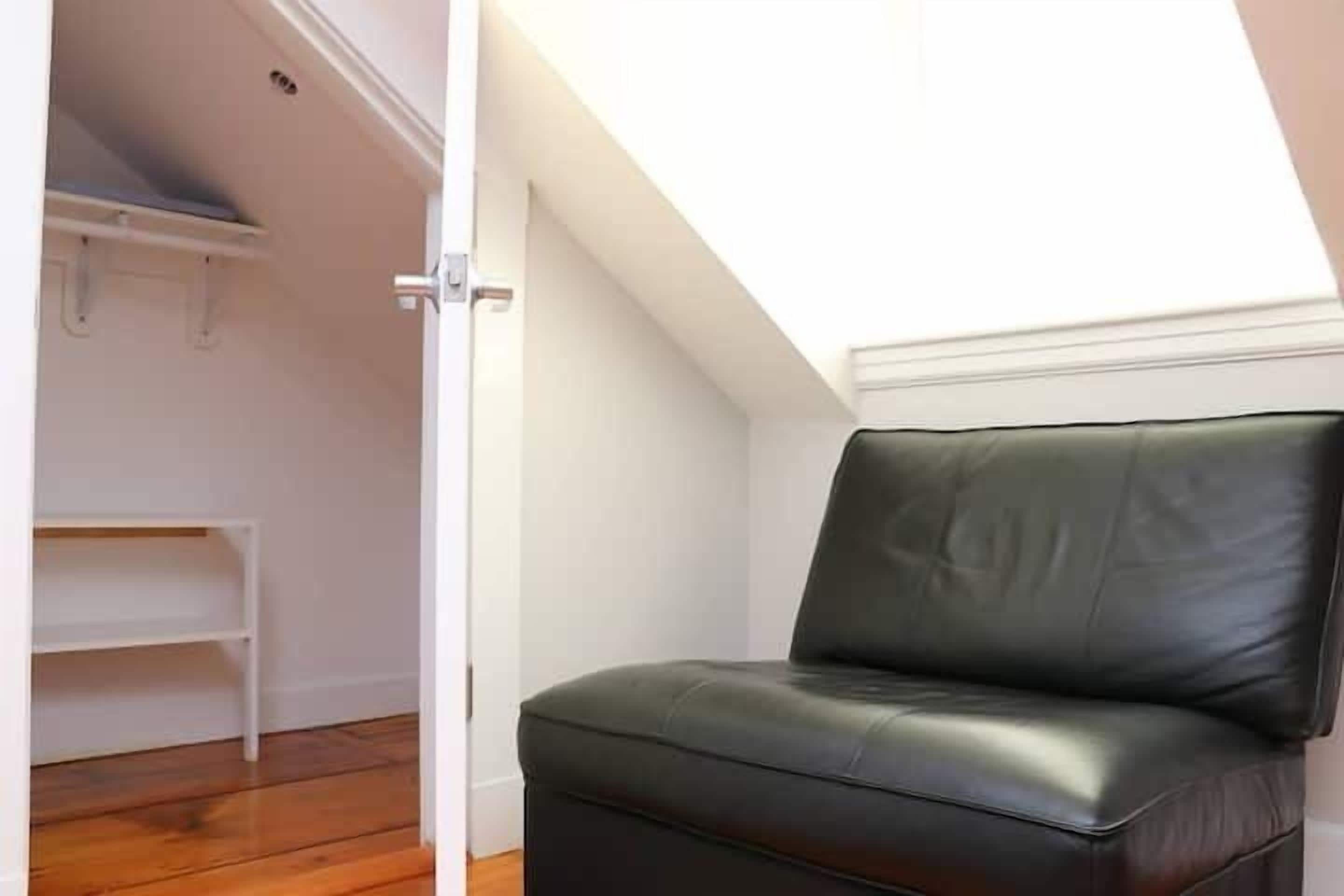 A room with a black leather chair, a white bench, and a white wall.