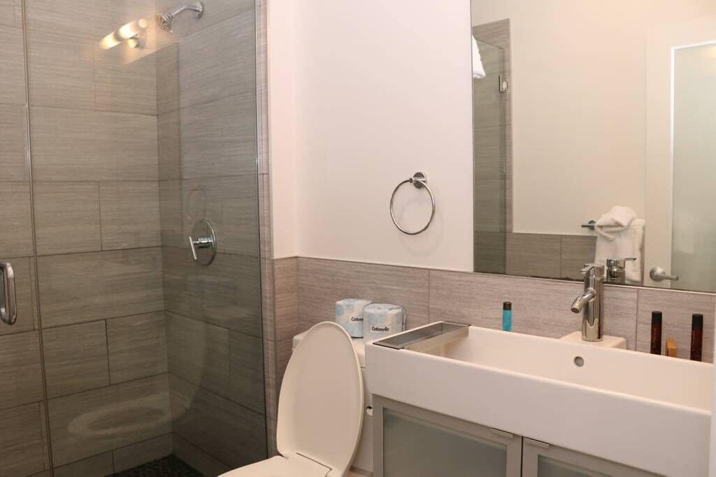Een moderne badkamer met een inloopdouche, toilet, wastafel en spiegel.