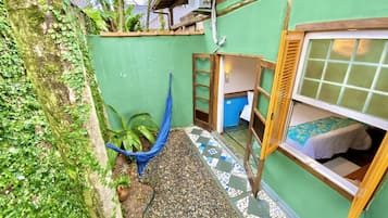 Zona exterior petita i tancada amb un hamaca, un llit amb col·fort de color blau i un paviment de rajoles.