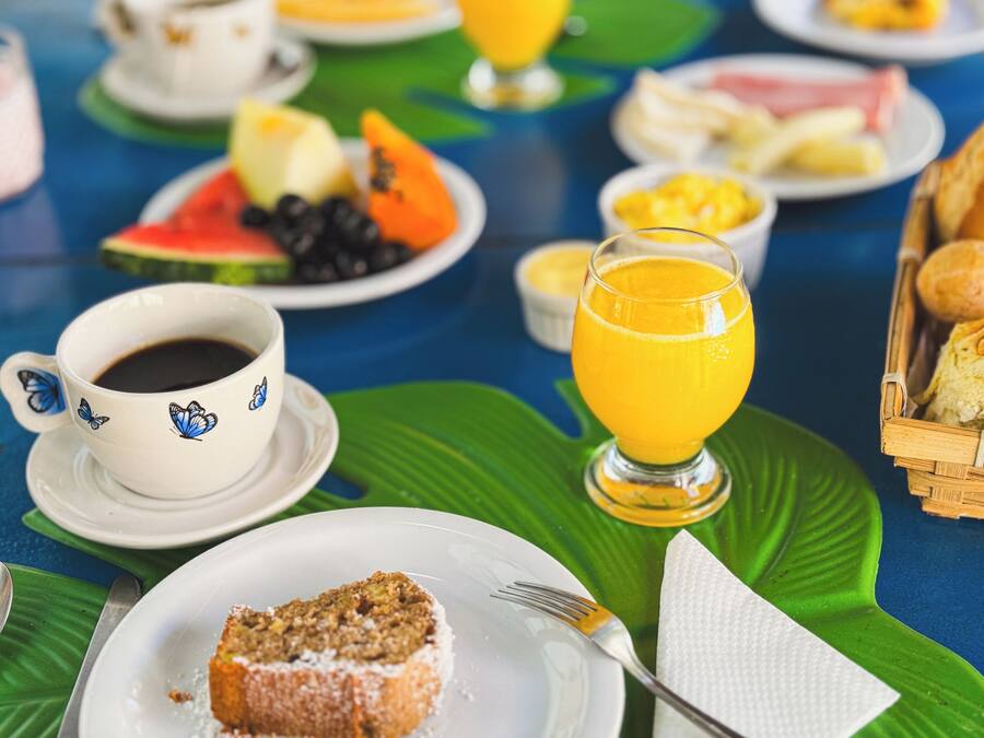 A breakfast setting with a variety of food items including a cup of coffee, a glass of orange juice, and a plate with a slice of cake.
