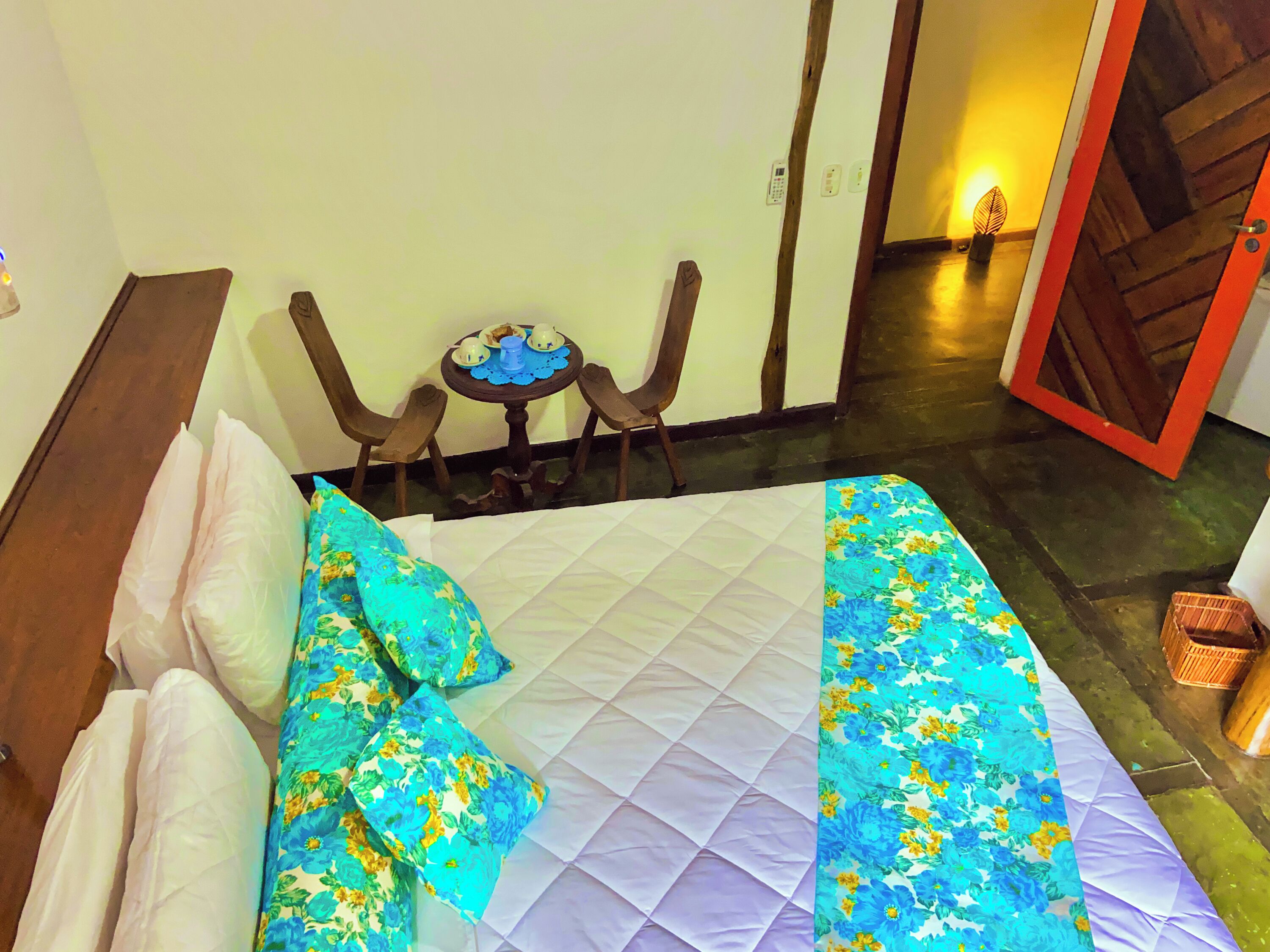 A bed with a floral bedspread, two pillows, and a small table with cups and a bottle.