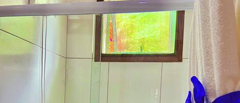 Un baño con azulejos blancos, una ventana con vistas a la vegetación y una toalla azul a la derecha.