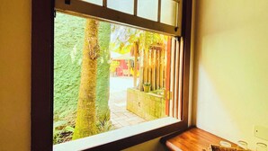 Una ventana con vista a un patio, una banca de madera y una pequeña mesa con vasos.