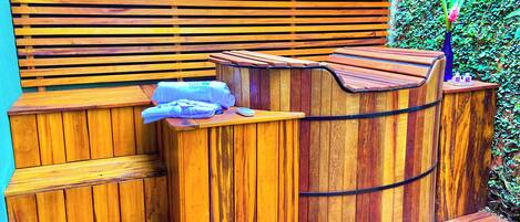 A wooden outdoor seating area with a bench and a wooden barrel.