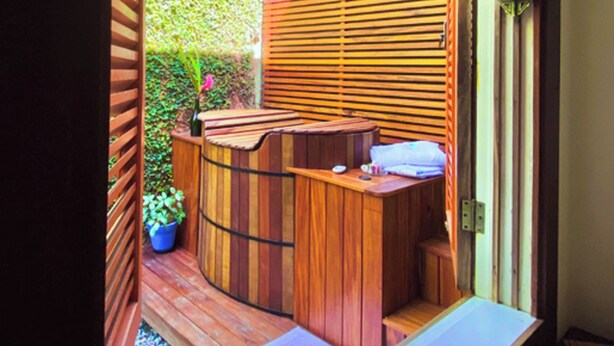 Zona de spa de madera con un banco, un lavamanos pequeño y una planta en maceta.