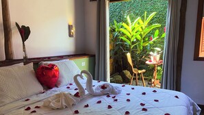 Una cama bien hecha con pétalos de rosa y una decoración de cisne, una caja de regalo roja y vistas de follaje a través de una ventana.