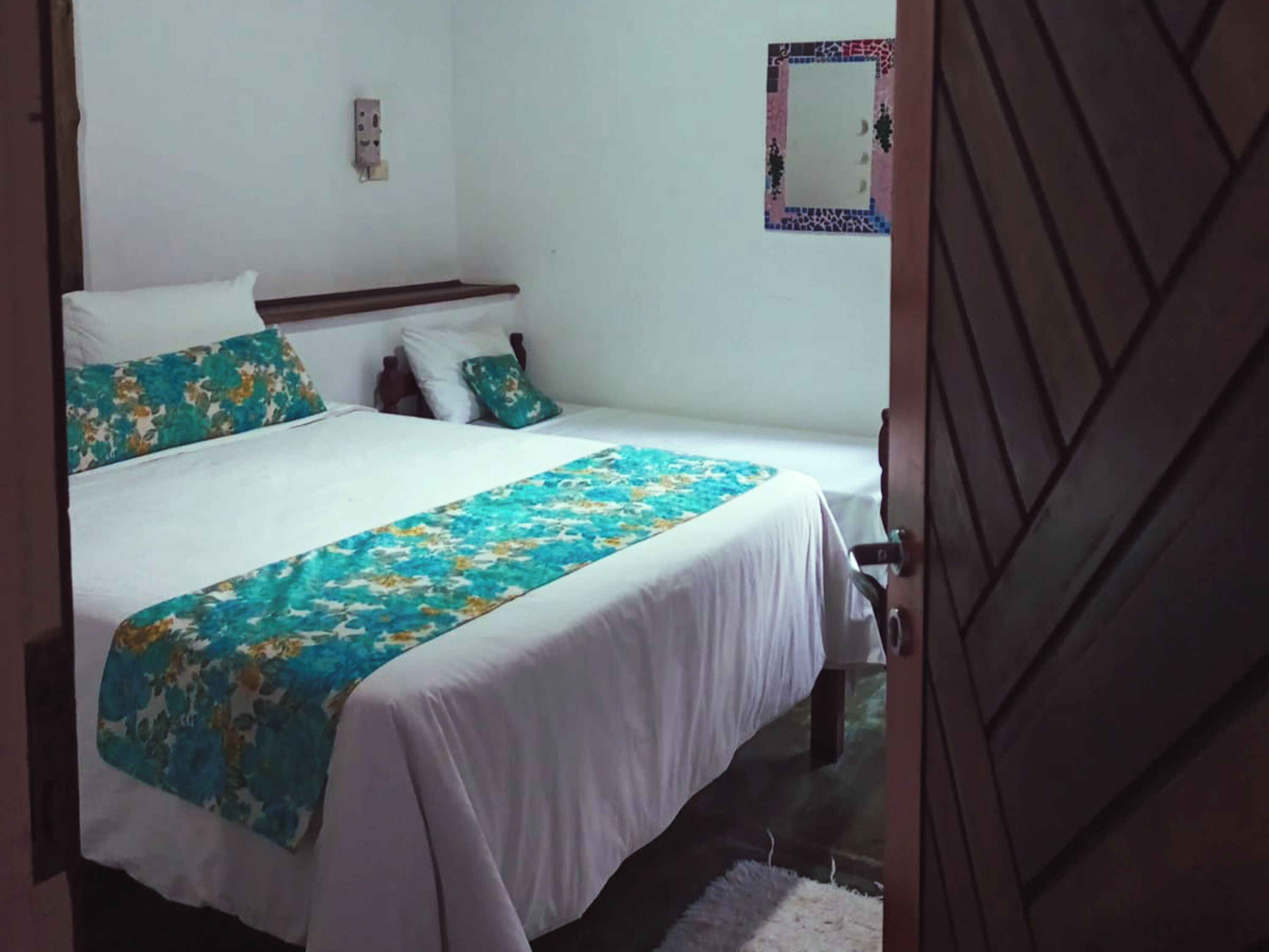 Quarto com duas camas de solteiro, cabeceira de madeira, roupa de cama branca e manta com padrão floral.