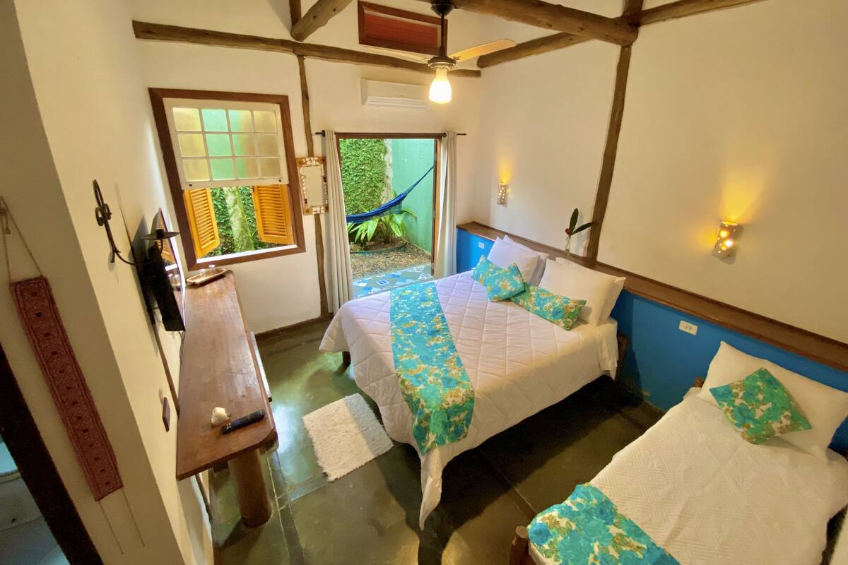 A room with two beds, a wooden desk, a hammock outside, and a ceiling fan.