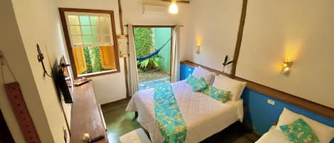 A room with two beds, a wooden desk, a hammock outside, and a ceiling fan.