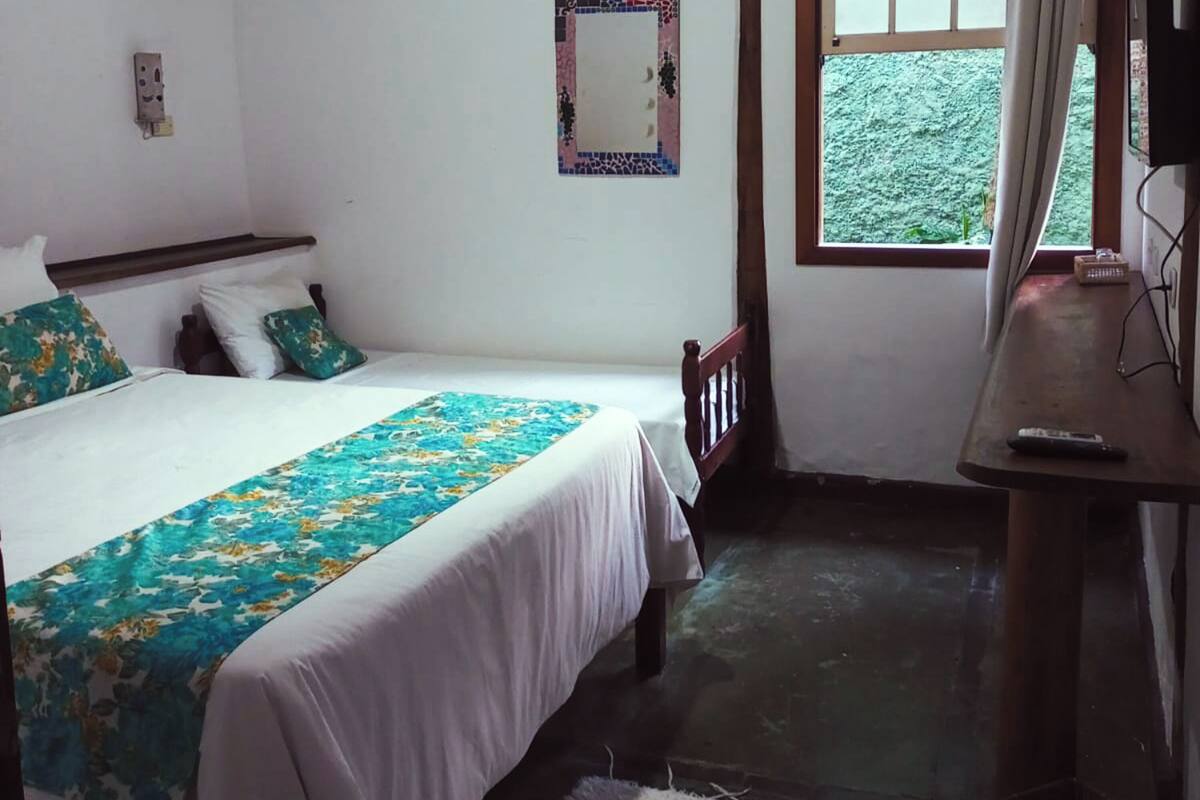 A bedroom with a bed, a wooden nightstand, a mirror, and a window with a view of greenery outside.
