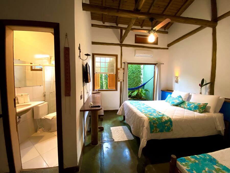 A room with a bed, a small table, a mirror, and a window with a view of greenery.