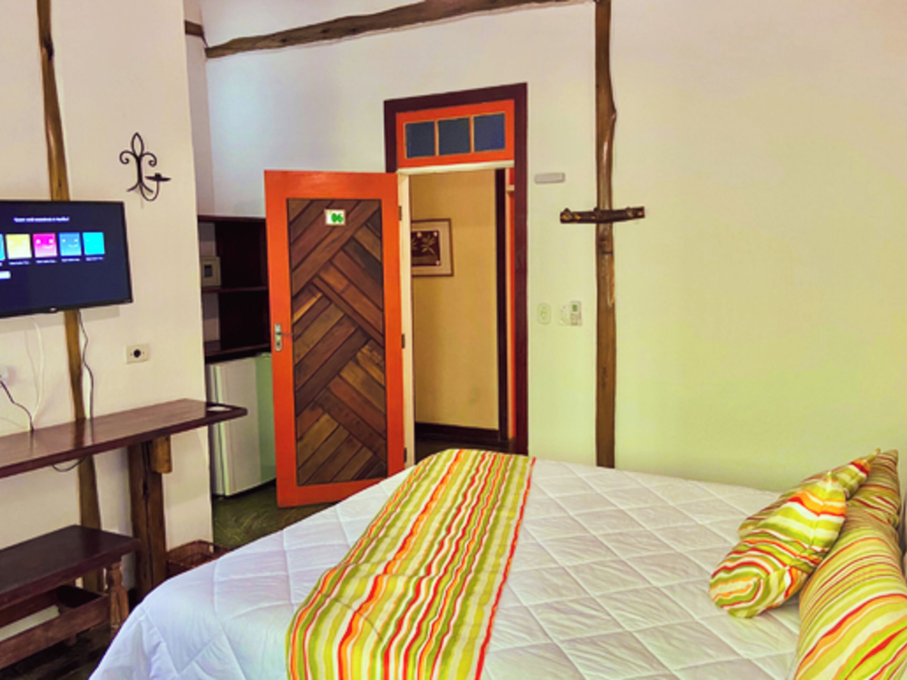 A hotel room with a bed, a television on a stand, and a door leading to another room.