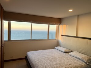 Een slaapkamer met een bed, een raam met uitzicht op zee en een plafondlamp.