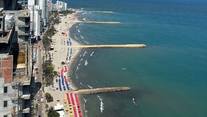 A coastal cityscape with a wide beach lined with colorful umbrellas, a clear blue sky, and high-rise buildings along the shore. - Enjoy the terrace and the best sunset and view of the city. (Cartagena de Indias)