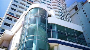 A tall, modern building with a curved glass facade and multiple balconies. - Enjoy the terrace and the best sunset and view of the city. (Cartagena de Indias)