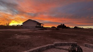 Een huis met veranda, omgeven door een droog landschap en een zonsondergang.