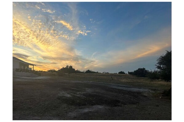 A rural landscape with a dirt road, a building on the left, and a clear sky with clouds. - DarkSkies Hideaway an experience you will remember (Fredricksburg)