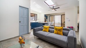 Una sala de estar moderna con un sofá gris, cojines amarillos, una mesa de centro de vidrio y un ventilador de techo.
