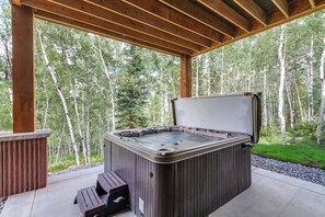 A hot tub in a covered outdoor area with a wooden deck and a view of a forest.
