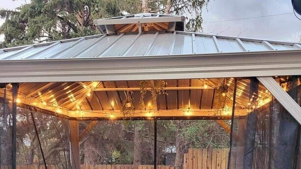 Un patio cubierto con mobiliario de mimbre, una chimenea y luces colgantes.