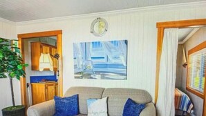A living room with a grey sofa, two blue cushions, a potted plant, a wooden cabinet, and a framed picture on the wall. - Historic Oceanfront Cottage in Charming Nye Beach (Newport)