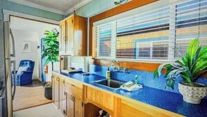 A kitchen with wooden cabinets, a blue countertop, a window with blinds, and a potted plant. - Historic Oceanfront Cottage in Charming Nye Beach (Newport)