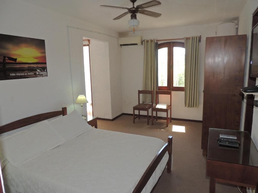 A hotel room with a bed, a desk, a chair, a ceiling fan, and a window with curtains.