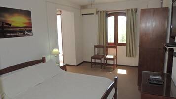 A hotel room with a bed, a desk, a chair, a ceiling fan, and a window with curtains.