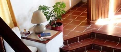 Un vestíbulo de hotel con una escalera, un mostrador de recepción, un área de descanso con una mesa y sillas, y una planta en maceta.