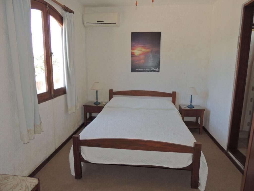 A bedroom with a wooden bed, two bedside tables with lamps, a window with curtains, and a poster on the wall.