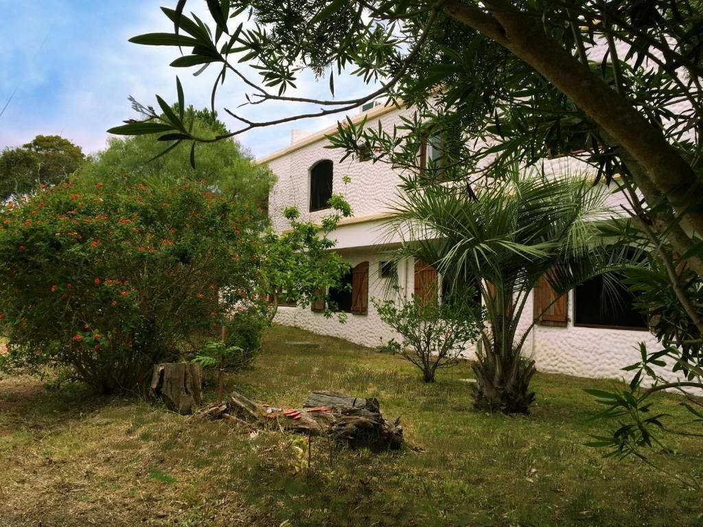 Un edificio bianco con tetto spiovente, circondato da vegetazione rigogliosa e un piccolo giardino.