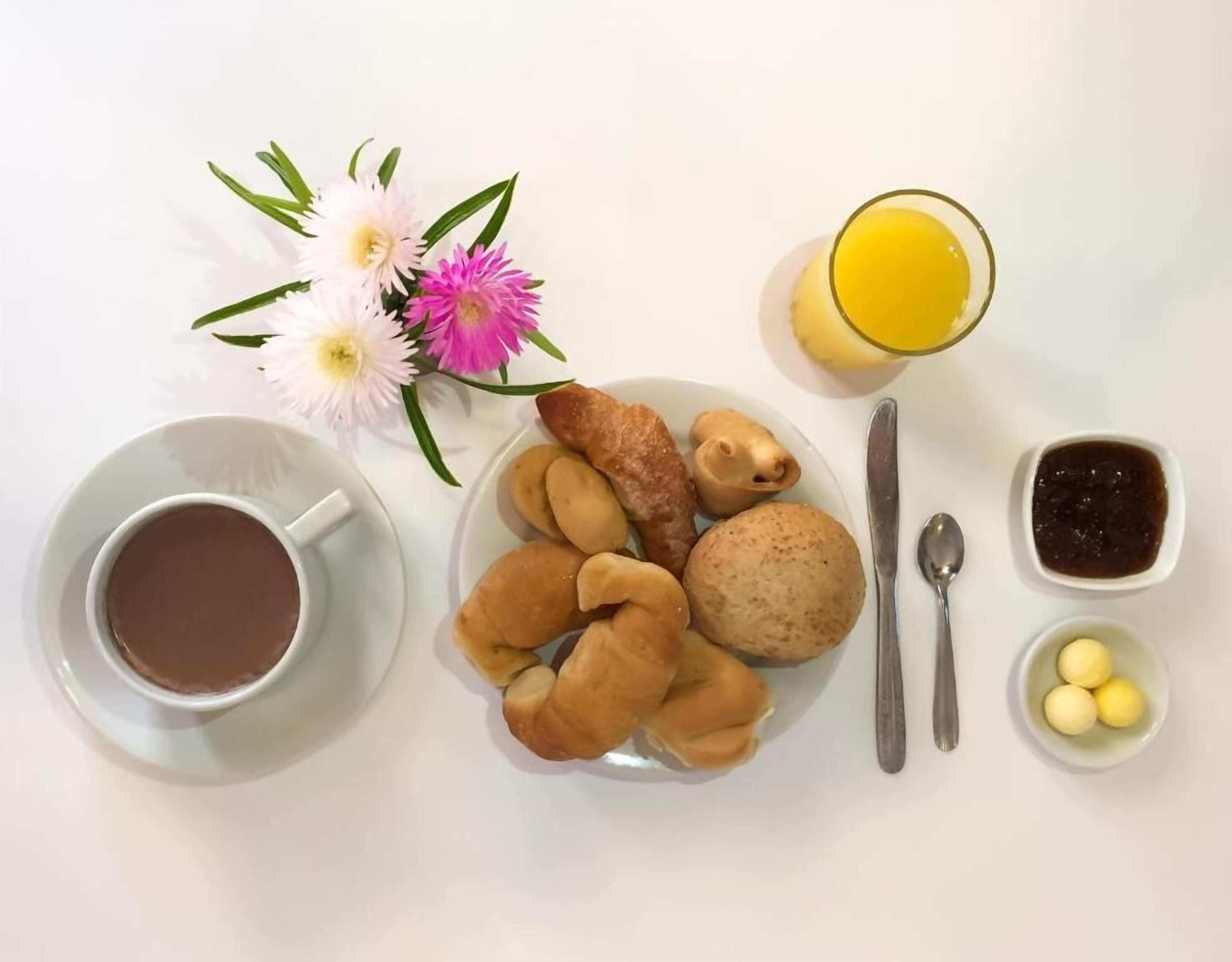 A breakfast setting with a plate of pastries, a cup of coffee, a glass of orange juice, and a small bowl of jam.