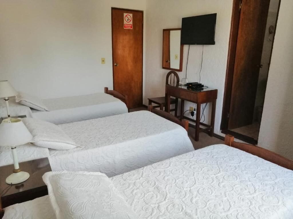 Habitación de hotel con dos camas individuales, un escritorio con silla, televisor montado en la pared y una puerta con letrero de prohibido fumar.